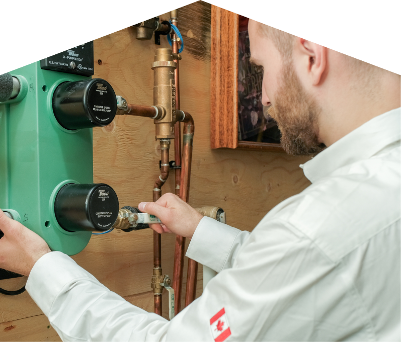 Furnasman HVAC specialist performing boiler installation, securing a valve on a new hydronic heating system with copper piping and a green circulation pump mounted on a wooden wall.