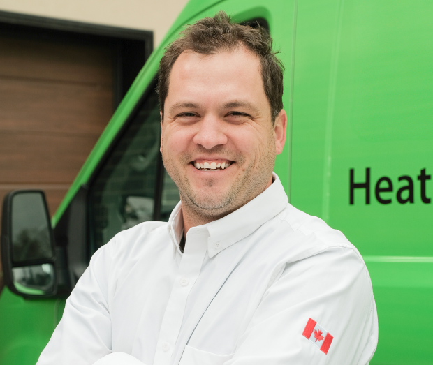 Smiling Furnasman technician standing confidently in front of their green service van, wearing their white issued uniform.