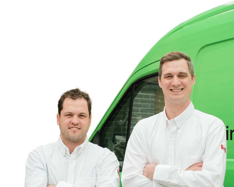 Two Furnasman technicians smiling in front of their green service van, wearing issued jackets during an on-site consultation.